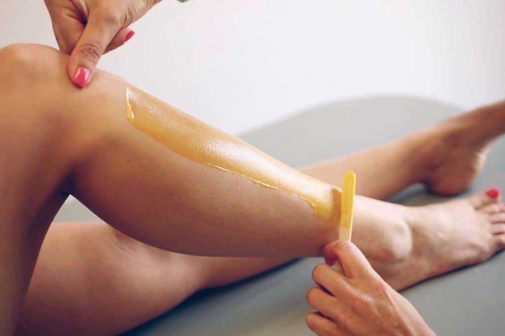 Female leg undergoing wax application with a spatula for hair removal on a massage table.