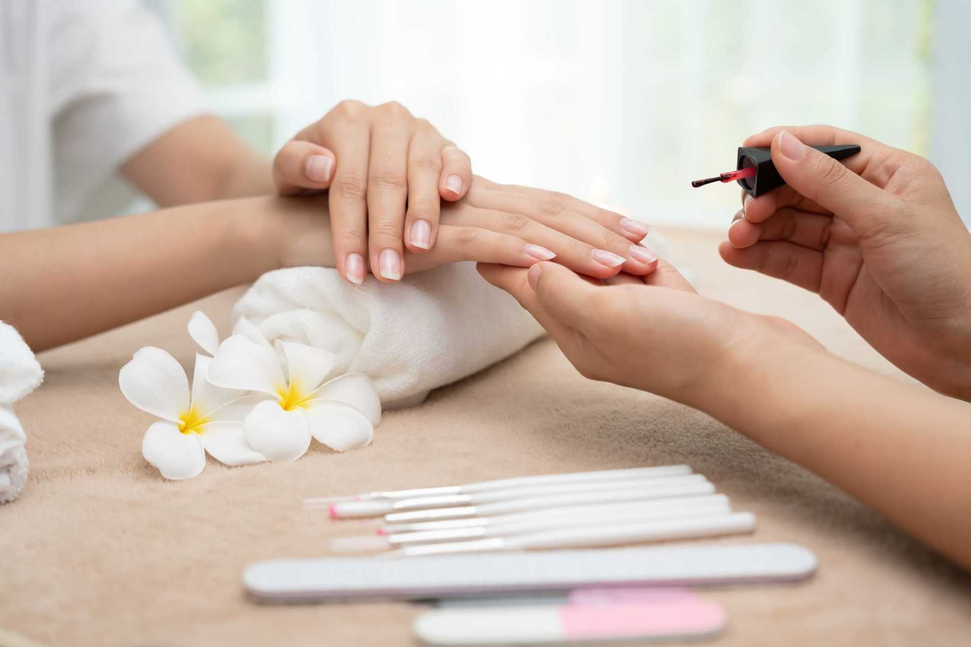 Nail technician applying polish with tools and flower on a towel.