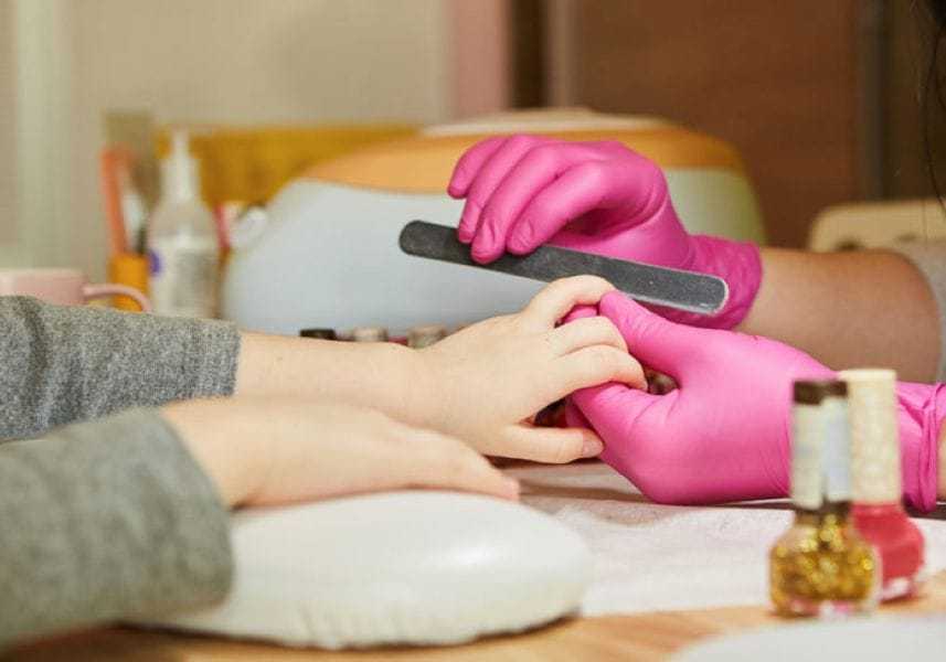 Manicure in progress with pink gloves; person filing nails on another's hand.
