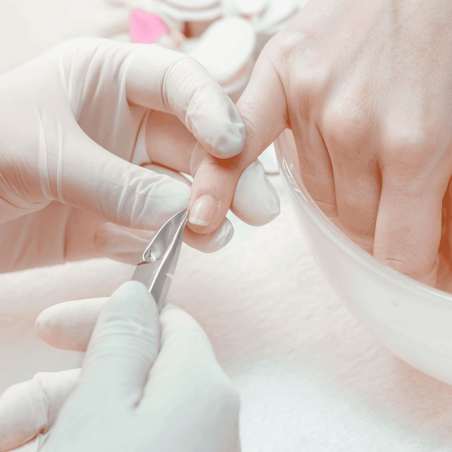 Manicure process: gloved hands working on a client's nails over a white surface.