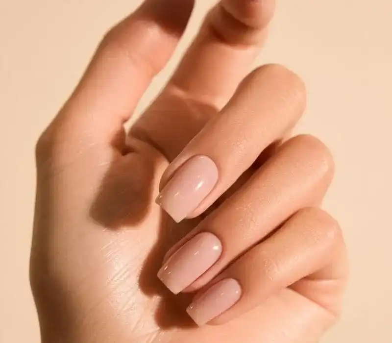 Women's hand with elegant nude manicure on a neutral background.